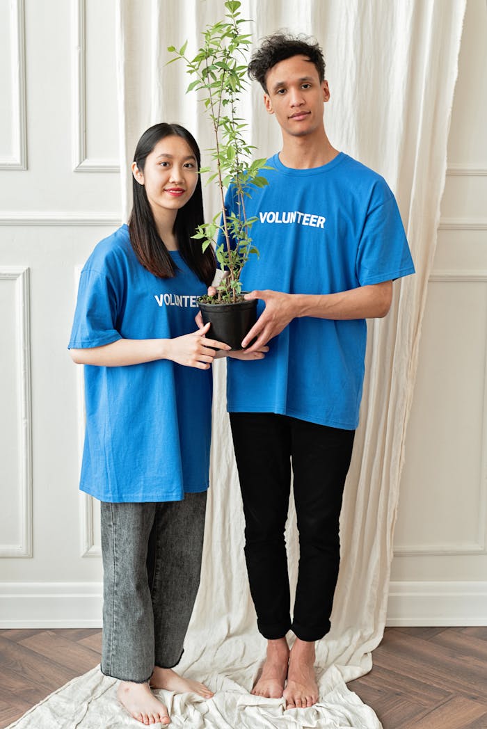 The Art of Drawing Readers In: Your attractive post title goes here Two volunteers in blue shirts holding a potted plant, promoting environmental sustainability.